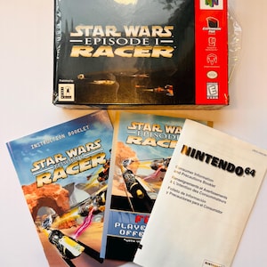 May include: A boxed copy of Star Wars Episode I Racer for the Nintendo 64, with the game box and instruction booklets. The box is black with gold lettering and a red side panel. The instruction booklets feature images of the game.