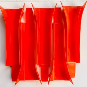 May include: Bright orange plastic objects arranged on a white surface. The objects have a unique, elongated shape with flared tops and rectangular bases. The arrangement suggests a design or decorative element, with the vibrant color making them visually striking.
