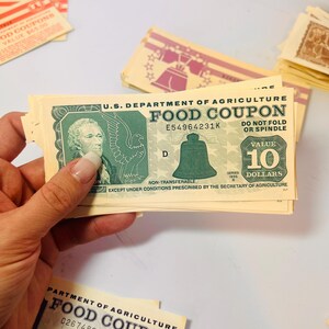 May include: A stack of U.S. Department of Agriculture Food Coupons, with a $10 value visible. The coupons feature an image of the Liberty Bell and the text "Food Coupon". Other coupons with different values are also present.