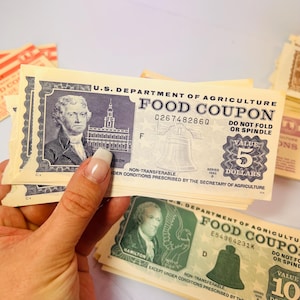 May include: A stack of vintage U.S. Department of Agriculture Food Coupons. The $5 and $10 coupons feature portraits of historical figures, the Liberty Bell, and the text "DO NOT FOLD OR SPINDLE".