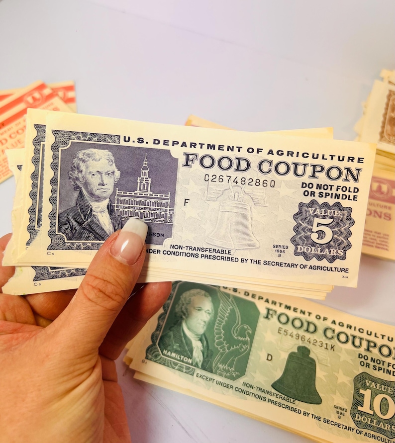 May include: A stack of vintage U.S. Department of Agriculture Food Coupons. The $5 and $10 coupons feature portraits of historical figures, the Liberty Bell, and the text "DO NOT FOLD OR SPINDLE".