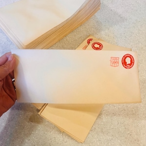 May include: A stack of cream-colored envelopes, with a hand holding one. The envelope has a red stamp that reads "2 CENTS" and a profile image. Several other envelopes are visible, some with the same stamp.