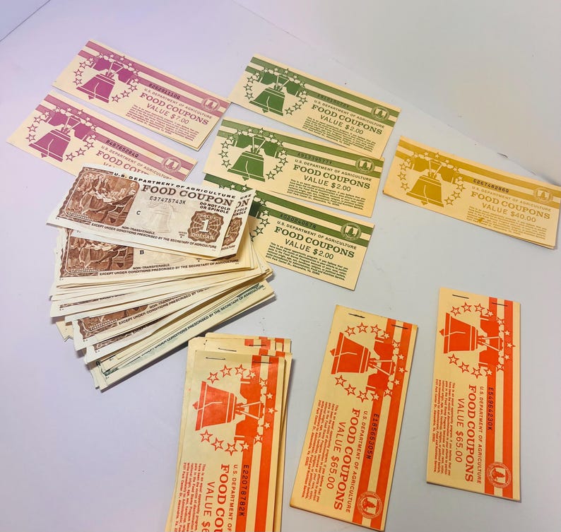 May include: Assortment of vintage U.S. Department of Agriculture food coupons in various colors. Coupons feature a Liberty Bell graphic and text indicating values of $1.00, $2.00, $7.00, $40.00, and $65.00. Some coupons are stacked.