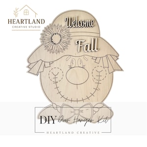 May include: A wooden DIY door hanger kit in the shape of a scarecrow. The scarecrow has a hat with the words "Welcome Fall" and a sunflower. The kit includes a bow tie and stitched details. The text "DIY Door Hanger Kit" is also included.