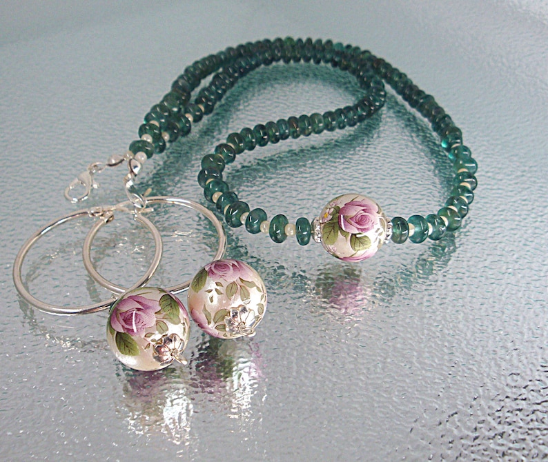 Pu&ograve; includere: Un set di orecchini a cerchio d'argento con perline a motivi floreali e una collana abbinata con perline verdi. La collana ha una perlina pi&ugrave; grande a motivi floreali al centro.
