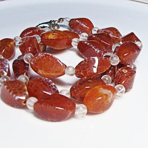Peut inclure: Un collier composé de perles d'agate orange avec des perles d'agate blanches intercalées.