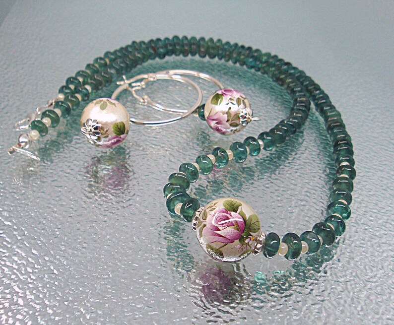 Pu&ograve; includere: Una collana di pietre preziose verdi con perline a motivi floreali e orecchini abbinati. La collana e gli orecchini sono realizzati in argento.