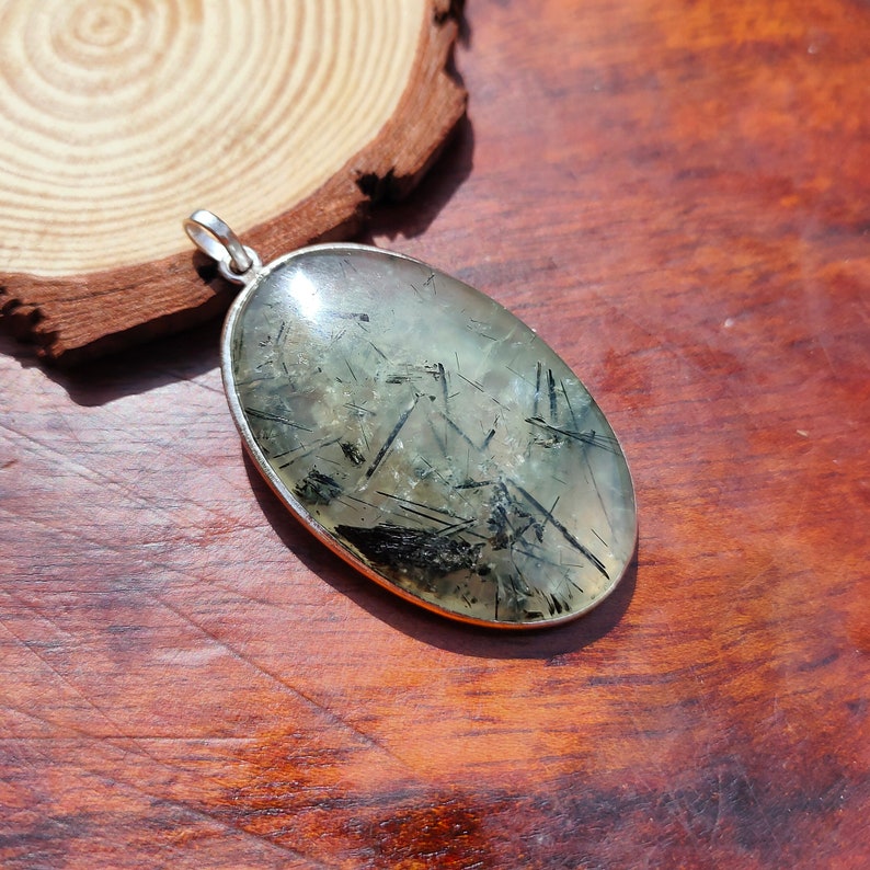 May include: Silver pendant featuring a clear oval-shaped stone with black inclusions. The stone has a natural, raw look and is set in a silver bezel.