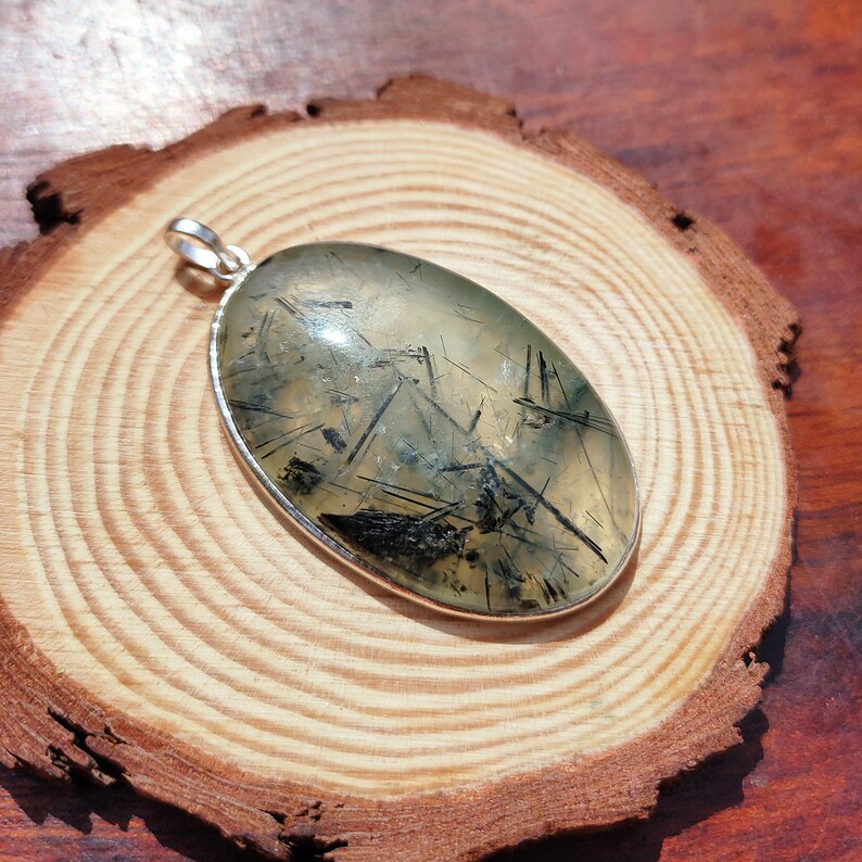 May include: Silver pendant featuring a clear quartz stone with black tourmaline inclusions. The oval-shaped stone is set in a silver bezel.