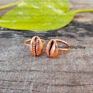 May include: Two copper rings with a seashell design. The rings are on a wooden surface.