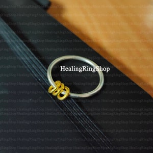 Könnte beinhalten: Ein silberner Ring mit drei goldenen Ringen, die daran befestigt sind. Die Ringe befinden sich auf einem schwarzen Hintergrund mit dem Text "HealingRingShop", der wiederholt wird.