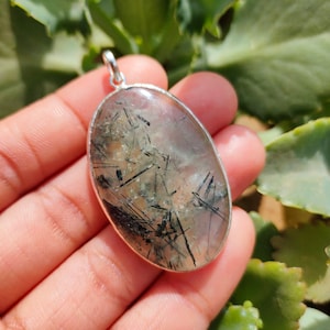 May include: Silver pendant featuring a clear quartz stone with black tourmaline inclusions. The oval-shaped stone is set in a silver bezel.