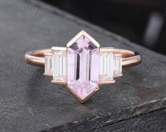 Puede incluir: Un anillo de compromiso de oro rosa con una piedra preciosa de talla esmeralda rosa rodeada de tres diamantes de talla baguette más pequeños.