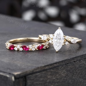 Peut inclure: Une bague de fiançailles en or avec un diamant taille marquise et une bande assortie avec des accents de rubis rouges.