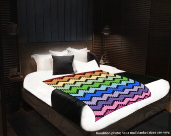 May include: A rainbow chevron crochet blanket on a white bed with black pillows.  The blanket is made with a variety of colors, including red, orange, yellow, green, blue, indigo, and violet.  The blanket is folded in half and placed on the bed.  The bed is in a dark room with a black headboard and a black nightstand.