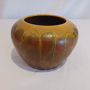 May include: A brown ceramic vase with a yellow glaze and green and red accents. The vase has a rounded shape and a wide opening.