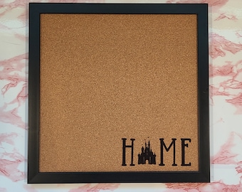 May include: A black framed corkboard with a brown cork surface. The word "HOME" is written in black letters with a silhouette of a castle in the middle of the word.