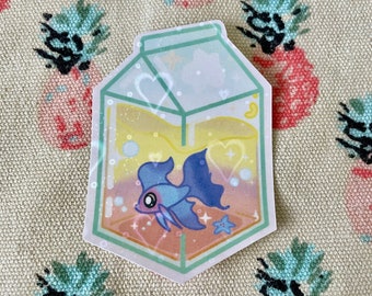May include: A sticker featuring a blue fish with flowing fins inside a milk carton. The carton has a light green outline and contains yellow and orange liquid with bubbles. A small blue starfish is next to the fish. The background is a beige fabric with pineapple designs.
