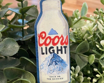 May include: A Coors Light beer can sticker with a blue mountain scene and the text "Cold as the Rockies".