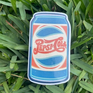 May include: A vintage-style sticker of a blue and red Pepsi-Cola can with a white background and a retro font.