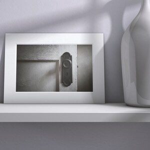 May include: A framed black and white photograph of a vintage door with a black door knob and keyhole. The door is made of wood and has a weathered look.