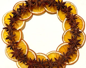 May include: A dried orange slice wreath decorated with star anise. The wreath is made of multiple dried orange slices, each with a star anise attached to it. The wreath is a natural, rustic, and festive decoration.