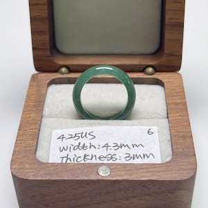 May include: A green jade ring displayed in a wooden box. The ring is a solid band with a polished finish. The text on the card reads: 4.25US, width: 4.3mm, thickness: 3mm. The ring is size 6.