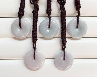 May include: Five jade pendant necklaces. Each pendant is a circular, pale green and lavender stone with a central hole. The pendants are suspended from dark brown braided cords.