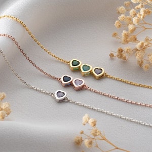 Op de afbeelding: Drie delicate gouden, roségouden en zilveren hartkettingen met kleurrijke edelsteenaccenten. Elke ketting heeft een ketting met drie hartbedels, elk met een edelsteen in een andere kleur.