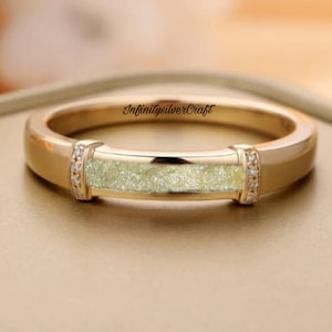 Puede incluir: Un anillo de banda de oro con una banda delgada de brillo verde y pequeñas piedras transparentes a cada lado. El anillo está grabado con el texto "InfinitySilverCraft".