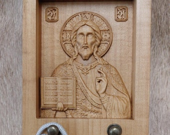 May include: A wooden religious icon featuring a carved image of Jesus Christ holding a book, with a silver rosary and crucifix in front. The rosary has silver beads and a St. Benedict medal.