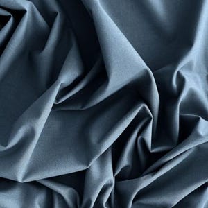 Könnte beinhalten: Nahaufnahme eines gefalteten Stoffes in einem gedämpften Blau-Grau. Der Stoff hat weiche Falten und Schatten, die ein Gefühl von Tiefe und Textur erzeugen. Das Material scheint ein mittelschwerer Webstoff zu sein, der für Kleidung oder Heimdekoration geeignet ist.