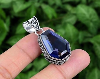 May include: A silver pendant with a large, faceted, dark blue gemstone set in a detailed silver frame. The pendant has a bail with a decorative design.