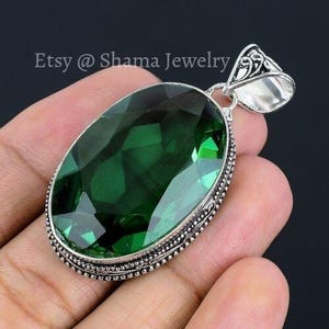 May include: A silver pendant with a large, faceted, oval-shaped green gemstone. The pendant has a detailed, ornate design around the gemstone.