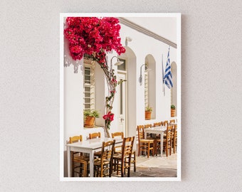 Könnte beinhalten: Ein weißes Gebäude mit einem rosafarbenen Bougainvillea-Strauch, der an der Seite hochwächst. Draußen stehen weiße Tische und Stühle, an der Wand hängt eine griechische Flagge.