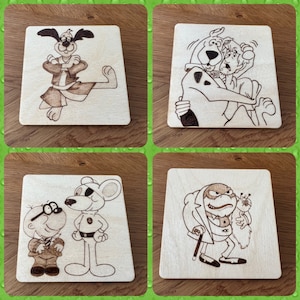 May include: Four wooden squares with different cartoon characters burned into the surface. The characters are a dog in a karate pose, a dog and a man, a mouse and a man, and a man with a cane and a small creature.