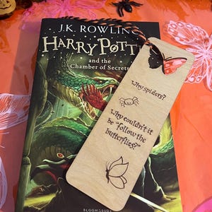 May include: A wooden bookmark with a butterfly design and the text "Why spiders? Why couldn't it be "follow the butterflies?"" on a Harry Potter book.