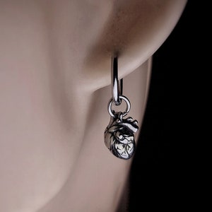 May include: Silver anatomical heart dangle earrings with a hoop design. The earrings are shown on a model's ear.