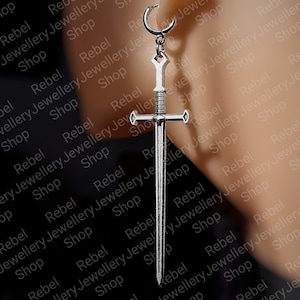 May include: Silver sword earring with a crescent moon hoop. The earring is worn in a person's ear.