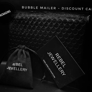 May include: Black bubble mailer with a black velvet pouch and a black discount card. The pouch and card both have white text that reads 'Rebel Jewellery' and the discount card also includes the website 'rebeljewelleryshop.com'.