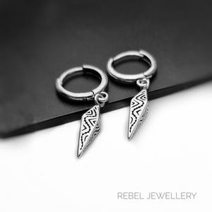 May include: A pair of silver hoop earrings with dangling, diamond-shaped pendants. Each pendant features a black and white geometric pattern. The earrings are displayed on a dark surface, with the text "REBEL JEWELLERY" visible in the bottom right corner.