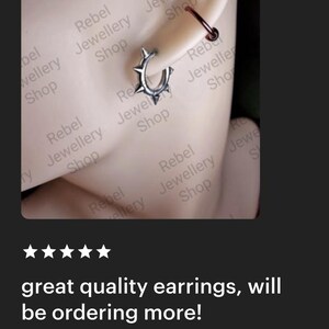 May include: A silver hoop earring with spike details is shown on an ear. A smaller, dark red hoop earring is also visible. The text "great quality earrings, will be ordering more!" is displayed below the earrings.