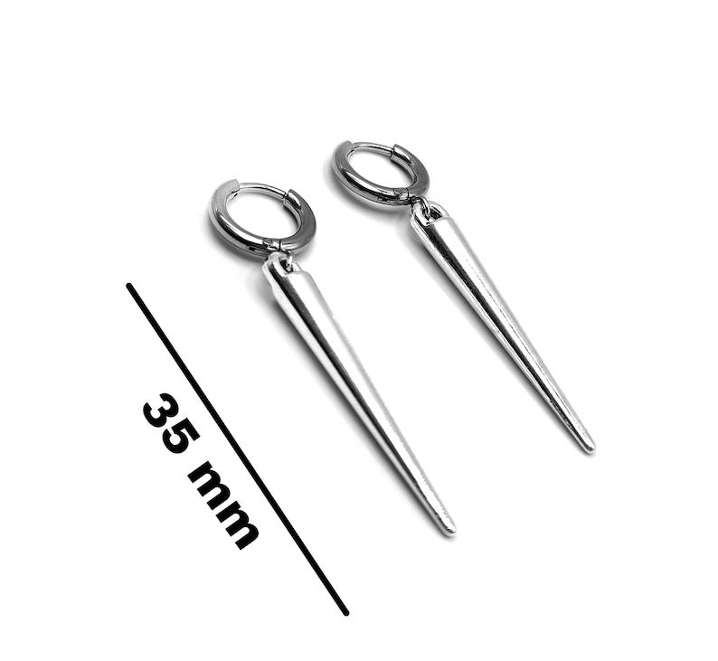 Puede incluir: Un par de pendientes de aro plateados con un colgante largo, c&oacute;nico y afilado. Los pendientes miden aproximadamente 3,5 cm de largo. Los pendientes se muestran sobre un fondo blanco.