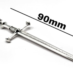 May include: A silver sword pendant with a 90mm length. The sword has a cross guard and a pointed tip.