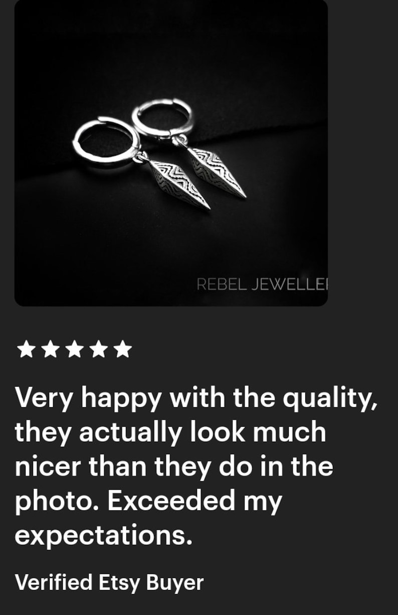 May include: Silver hoop earrings with dangling, pointed pendants. The pendants have a detailed, geometric design. The earrings are displayed on a dark background. The text "REBEL JEWELLEI" is visible.