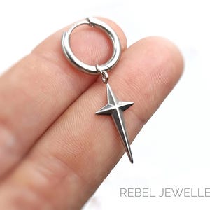 May include: A silver-colored hoop earring with a star pendant. The star has four points and hangs from the hoop. The earring is shown against a white background. The text "REBEL JEWELLERY" is visible at the bottom.