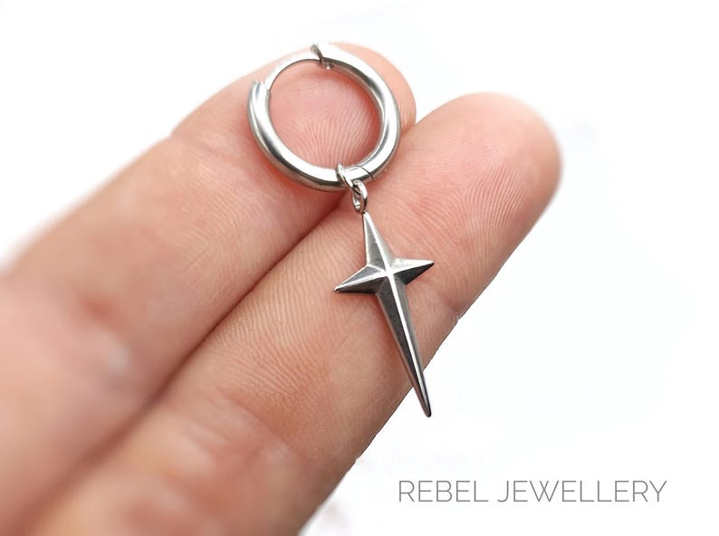 May include: A silver-colored hoop earring with a star pendant. The star has four points and hangs from the hoop. The earring is shown against a white background. The text "REBEL JEWELLERY" is visible at the bottom.