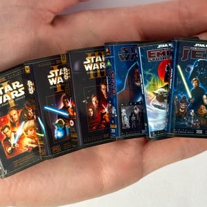 May include: A set of six miniature Star Wars VHS tape replicas featuring The Phantom Menace, Attack of the Clones, Revenge of the Sith, A New Hope, The Empire Strikes Back, and Return of the Jedi, each with detailed cover art and movie titles.