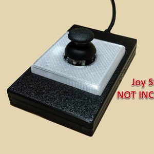 May include: A black joystick interface with a white plastic top and a black joystick knob. The text "Joy Stick NOT INCLUDED" is printed in red on the front of the interface.
