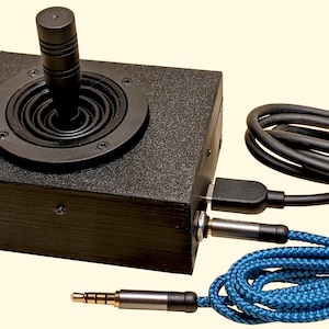 Könnte beinhalten: Ein schwarzer Joystick-Controller mit kreisförmiger Basis und zylindrischem Griff. Er hat ein USB-Kabel, eine 3,5-mm-Klinkenbuchse und ein blaues geflochtenes Kabel. Der Controller ist für Spiele oder andere interaktive Anwendungen konzipiert.